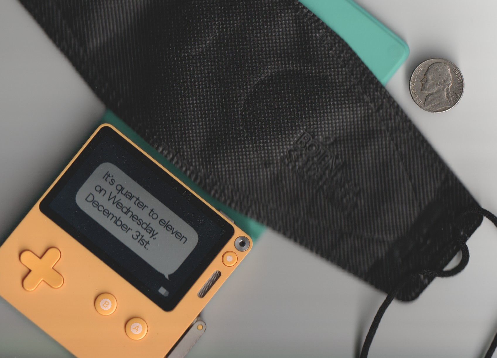 A flatbed scanner photo of a playdate, a mask, and a nickle laid about somewhat randomly, but in some sort of aesthetically pleasing way.